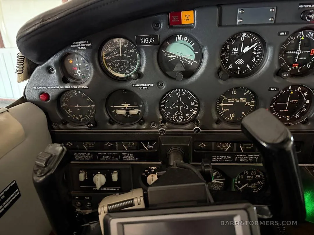 A close-up view of an aircraft's instrument panel, featuring analog gauges, a compass, and the registration N16JS above the airspeed indicator.