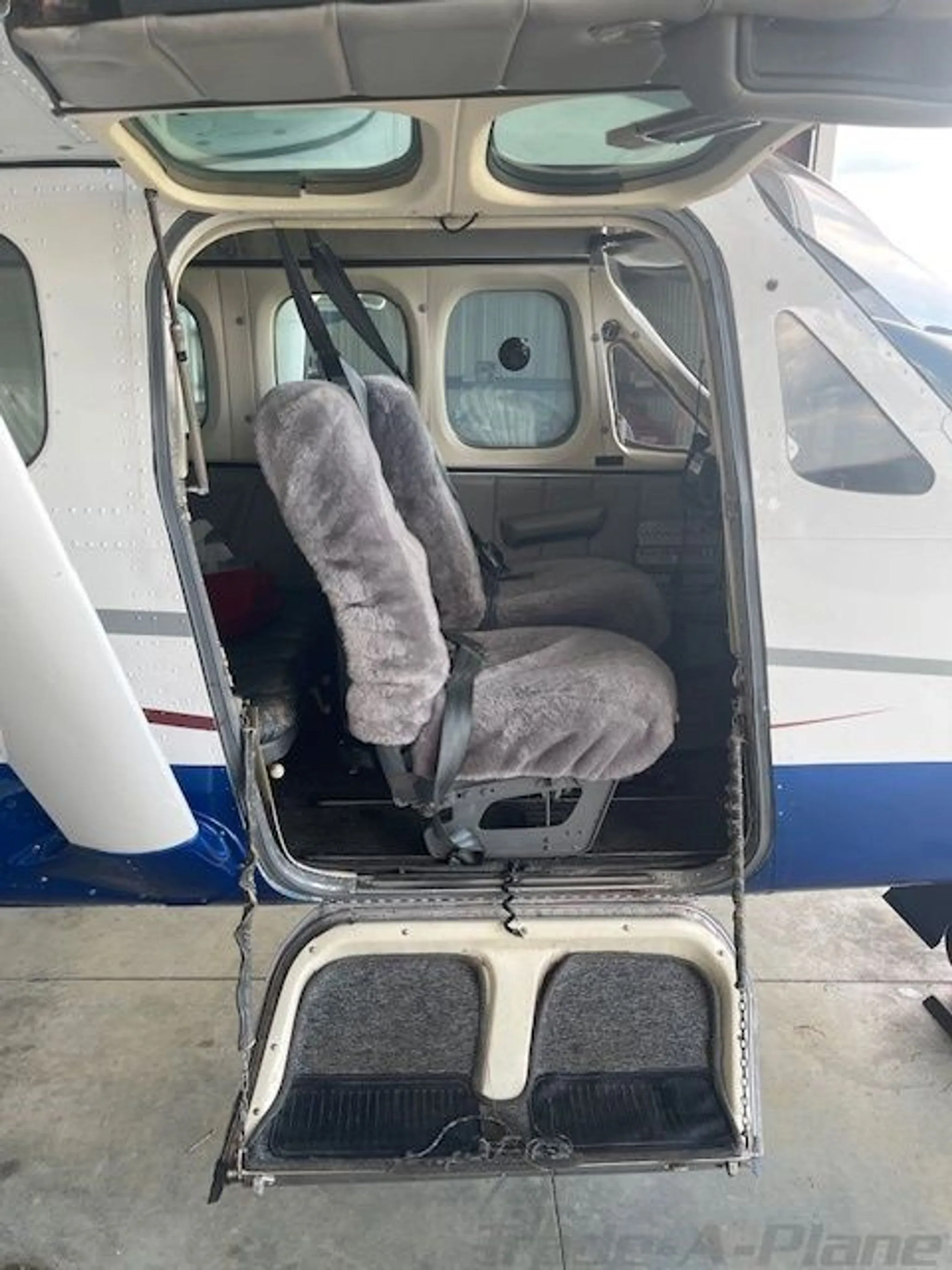 The open passenger door of the aircraft revealing two grey furry seat covers and the cabin interior.