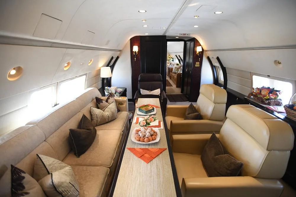 A luxurious aircraft cabin with a beige sofa, two armchairs, and a table laden with snacks.