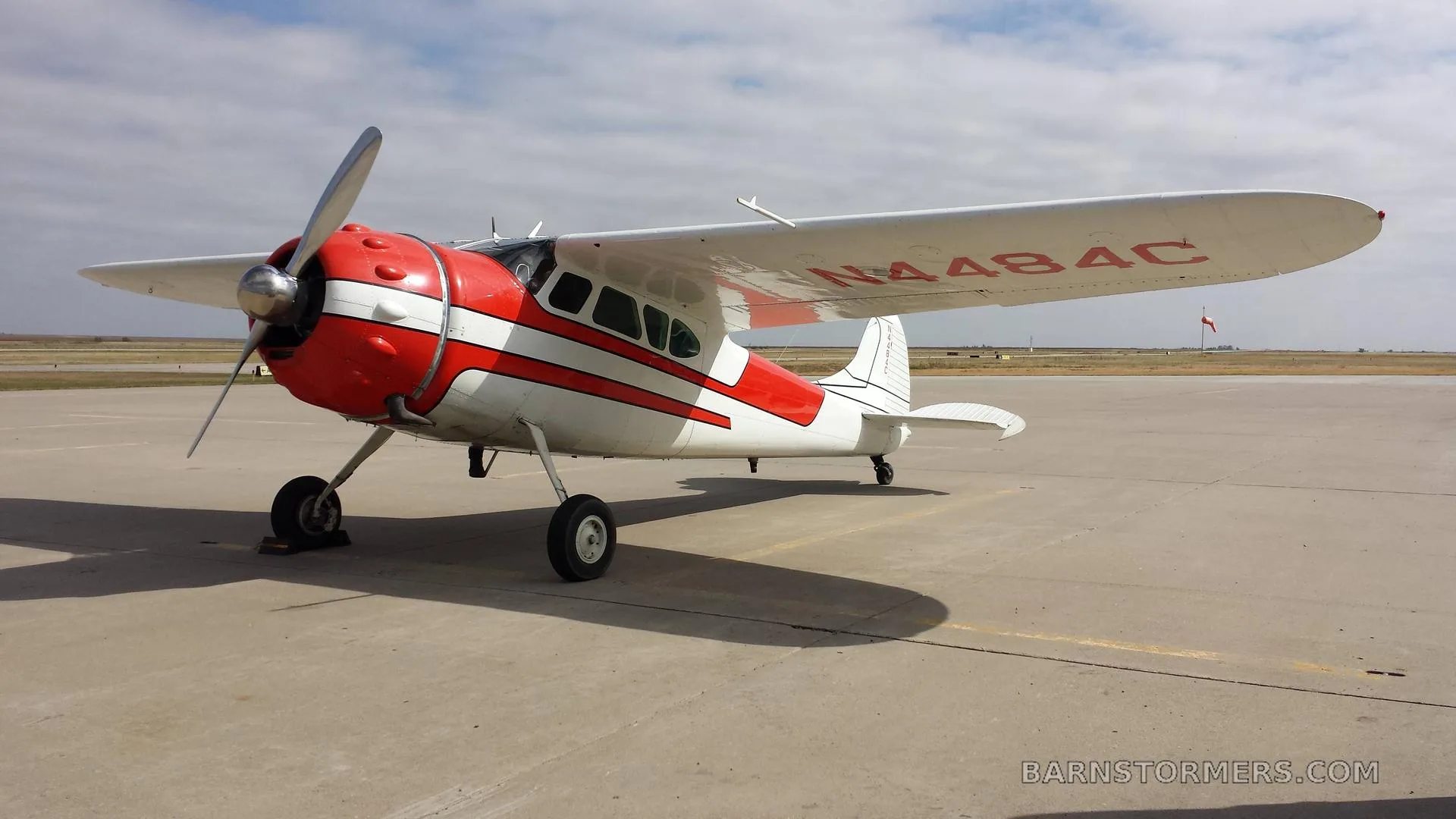 A red and white single-engine propeller aircraft with registration N484C parked on an asphalt runway under a partly cloudy sky.