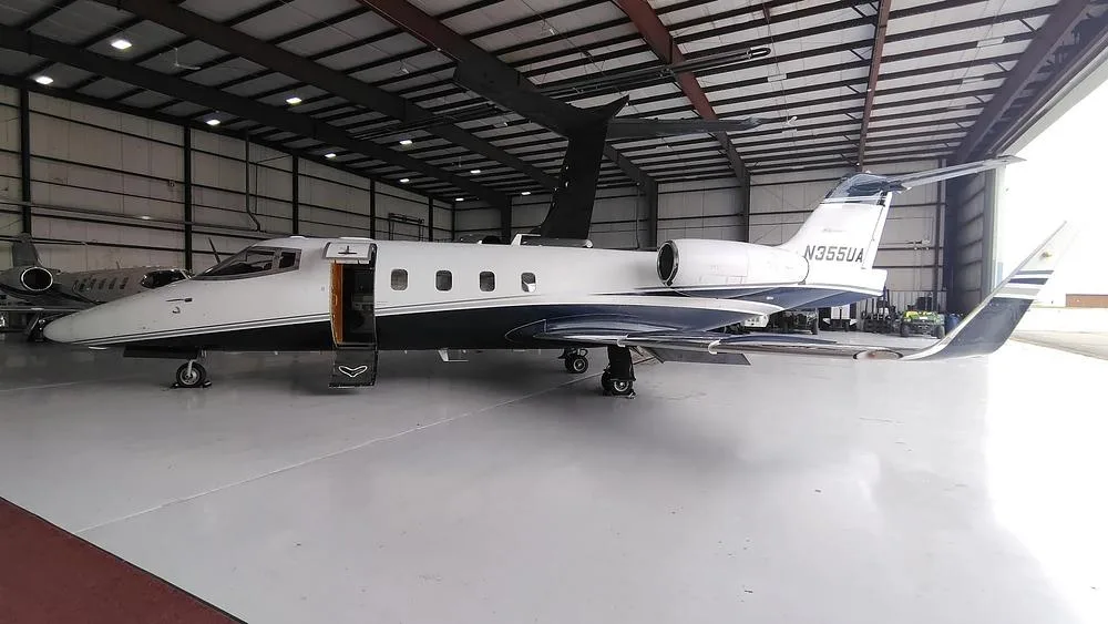 A white and dark blue private jet, N355UA, with its main door open, parked inside a hangar.