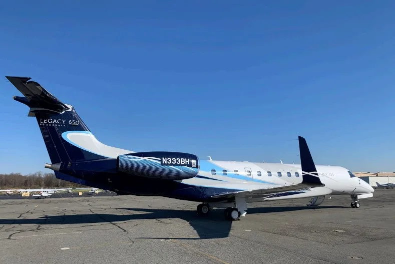 A side view of a white and dark blue Embraer Legacy 650 business jet with registration N333BH parked on an asphalt tarmac.