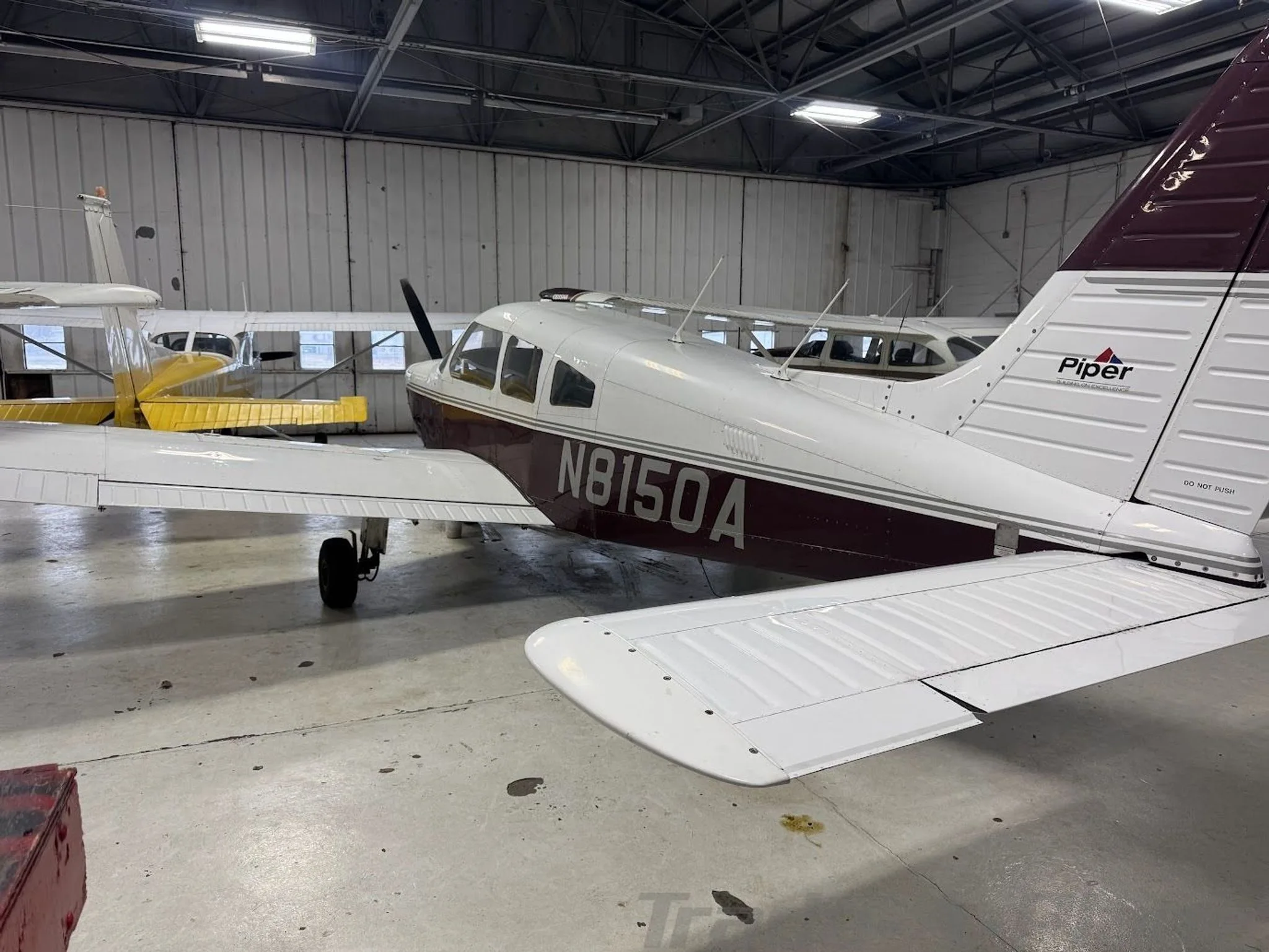 A white and maroon Piper Archer II (N8150A) parked in a hangar, viewed from the rear-right.