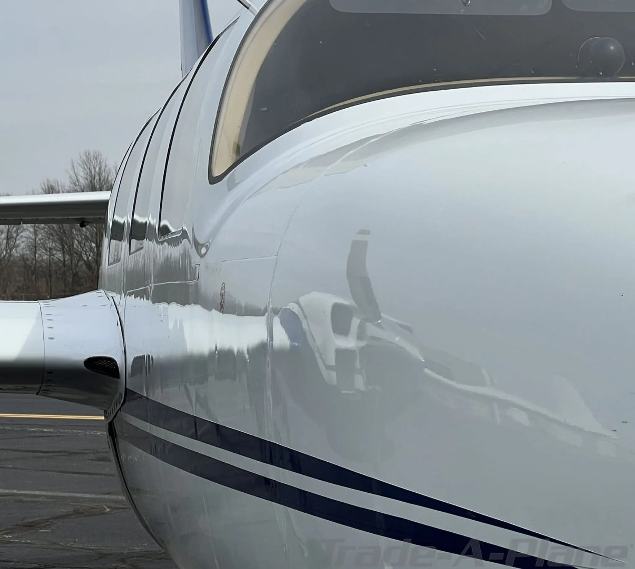 Close-up of the glossy white fuselage of the N25LL aircraft, reflecting the surroundings.