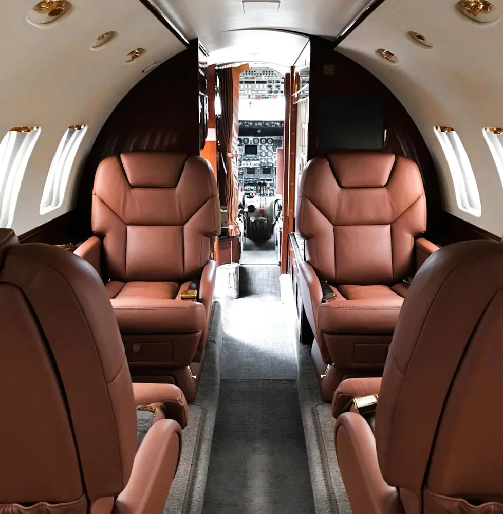 The luxurious interior cabin of a business jet with brown leather seats, looking forward towards the cockpit.