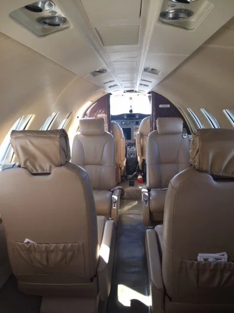 Aircraft cabin with tan leather seats and a view towards the cockpit.