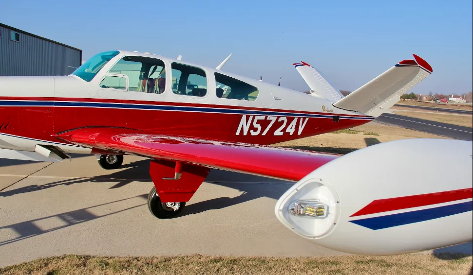 A close-up side view of the tail and wingtip of a red and white Beechcraft Bonanza N5724V.