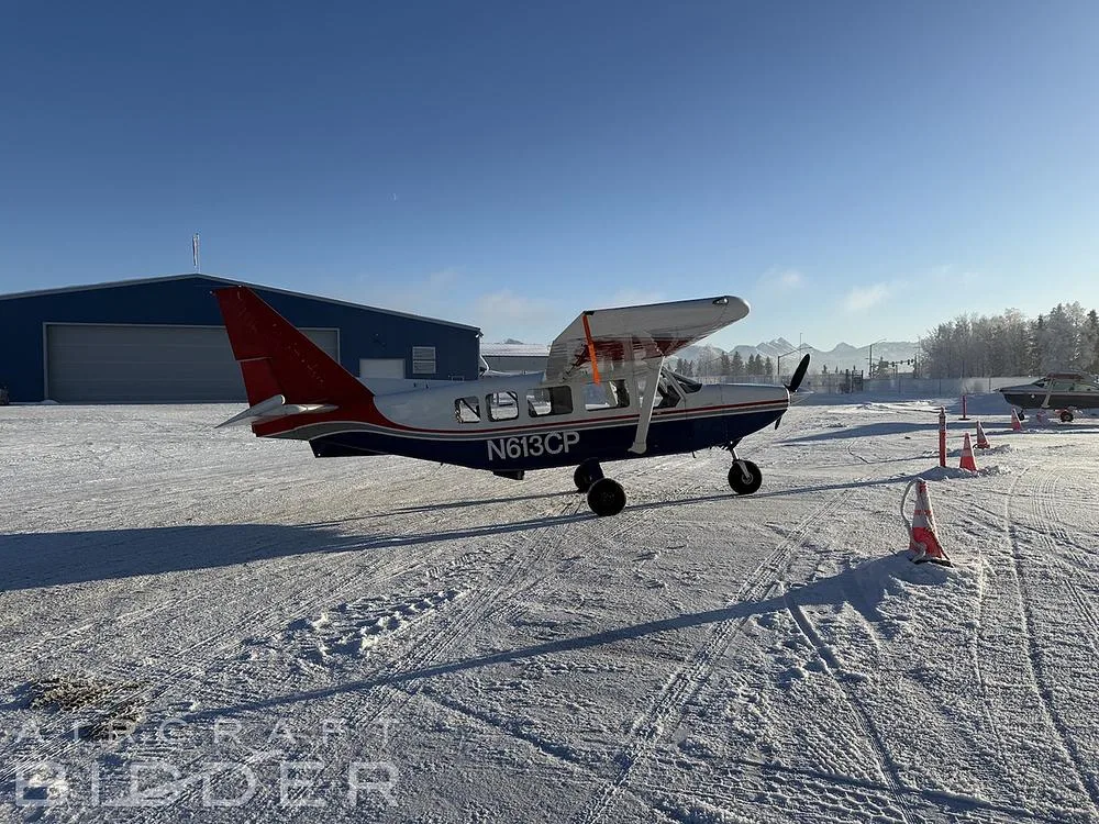 A side view of the N613CP Cessna 206, blue and white with red tail and wingtips, parked on a snowy airfield.