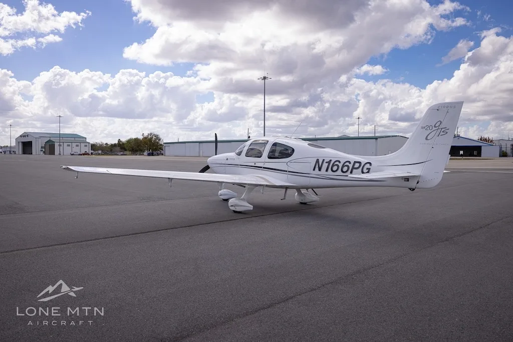 A rear-side view of the white Cirrus SR20 aircraft (N166PG) on an airport tarmac.