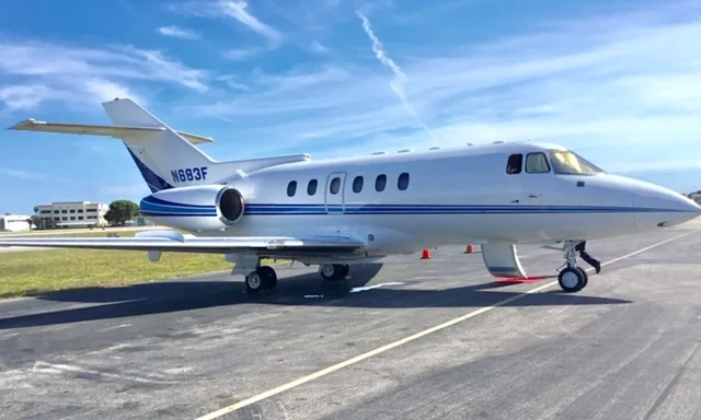 A white business jet with blue stripes (N683F) is parked on an airport tarmac under a blue sky.