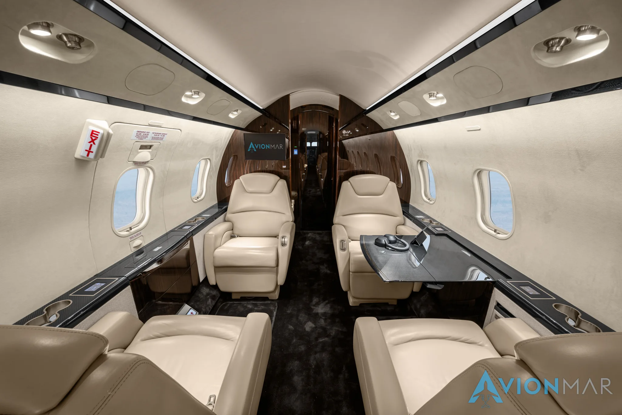 The luxurious interior of a private jet cabin with cream leather seats and a table, viewed from the rear.
