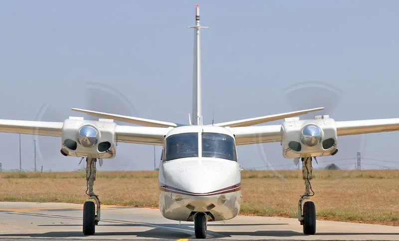 A white twin-engine aircraft with a maroon stripe on a tarmac, viewed from the front.