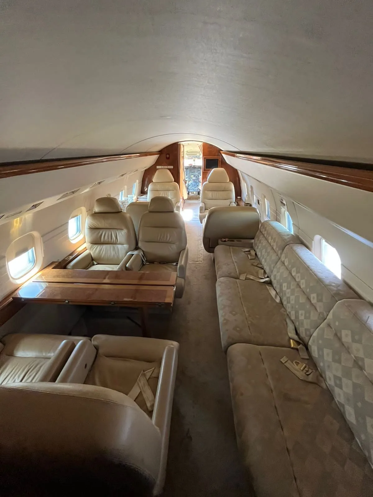 The interior cabin of a business jet, featuring beige leather seats, a wooden table, and a long patterned sofa.