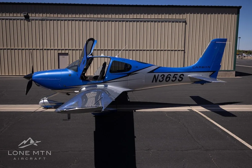 A side view of the blue and silver Cirrus SR22 aircraft, N365S, with its doors open, parked on an asphalt ramp.