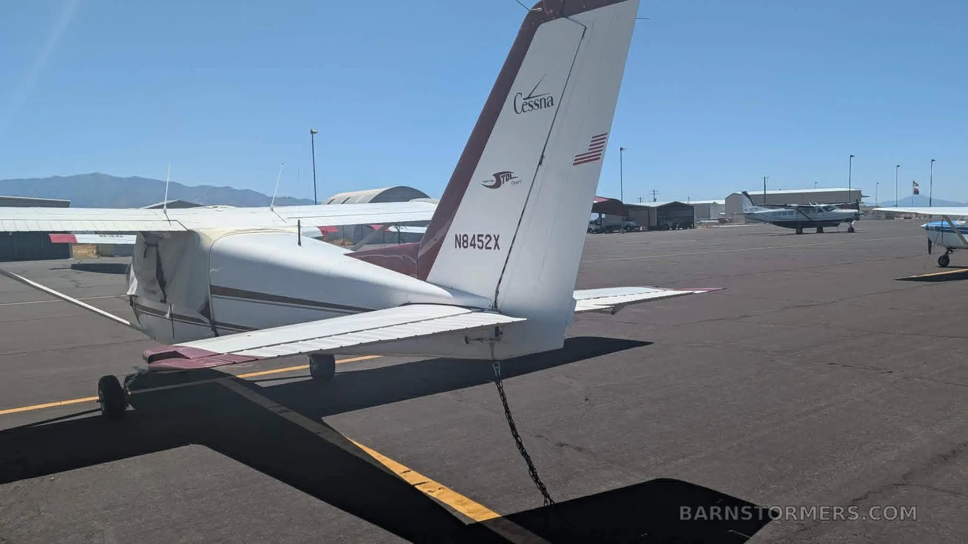 The tail section of a white and maroon Cessna aircraft with registration N8452X, parked on an airfield.