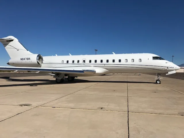 A white Bombardier Global Express business jet, registration N947BR, parked on a tarmac under a clear blue sky.