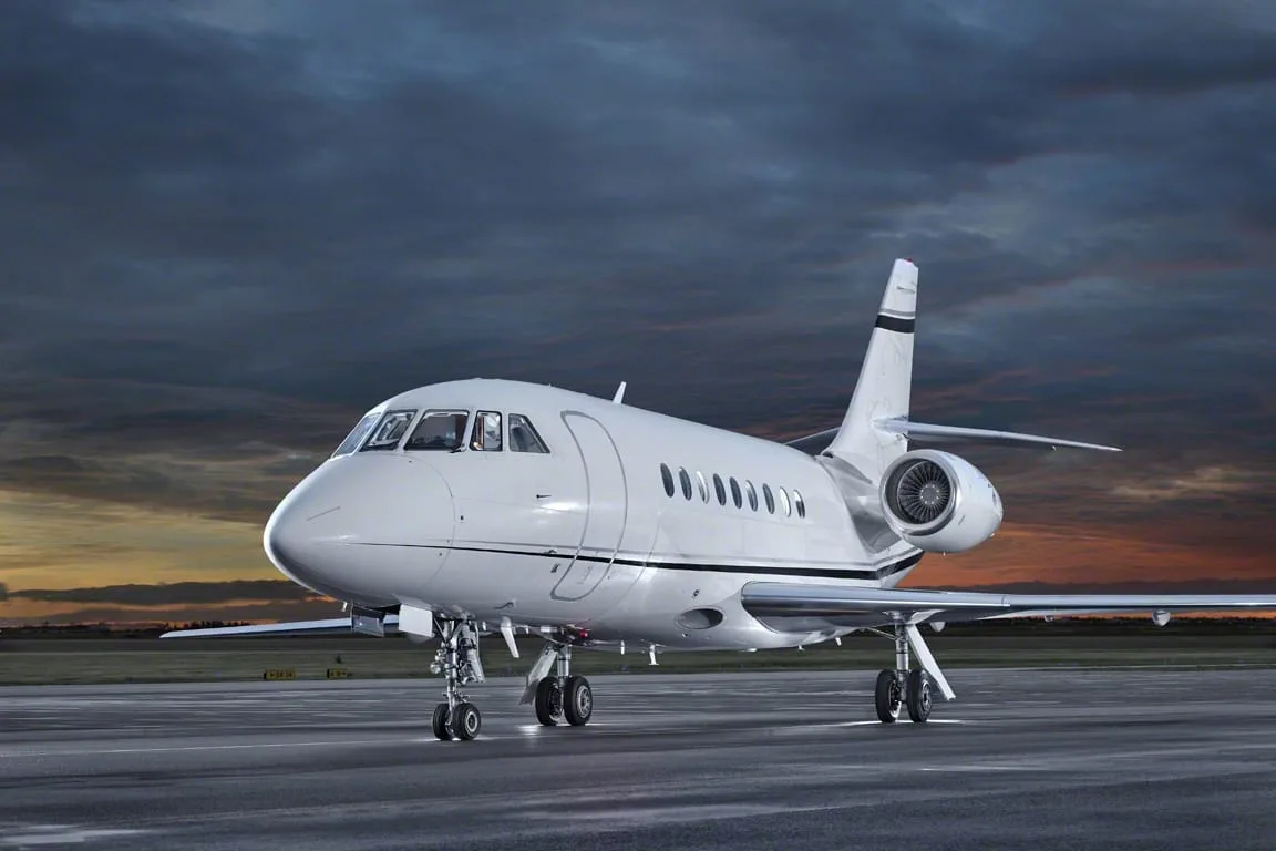 A white Dassault Falcon business jet parked on a runway at sunset.