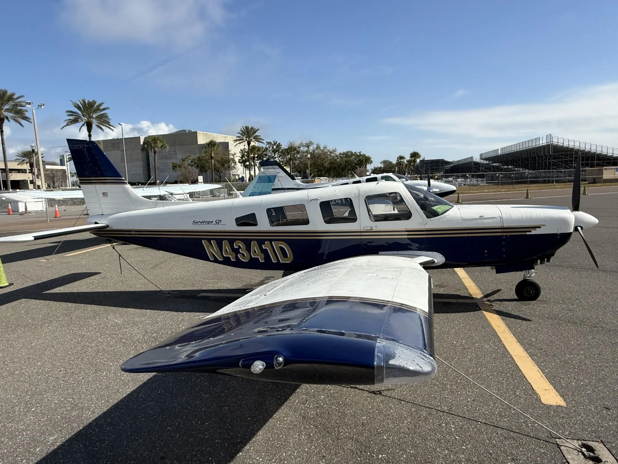 A Piper Saratoga SP (N4341D) in blue and white paint scheme parked on an airfield, viewed from the front-left.