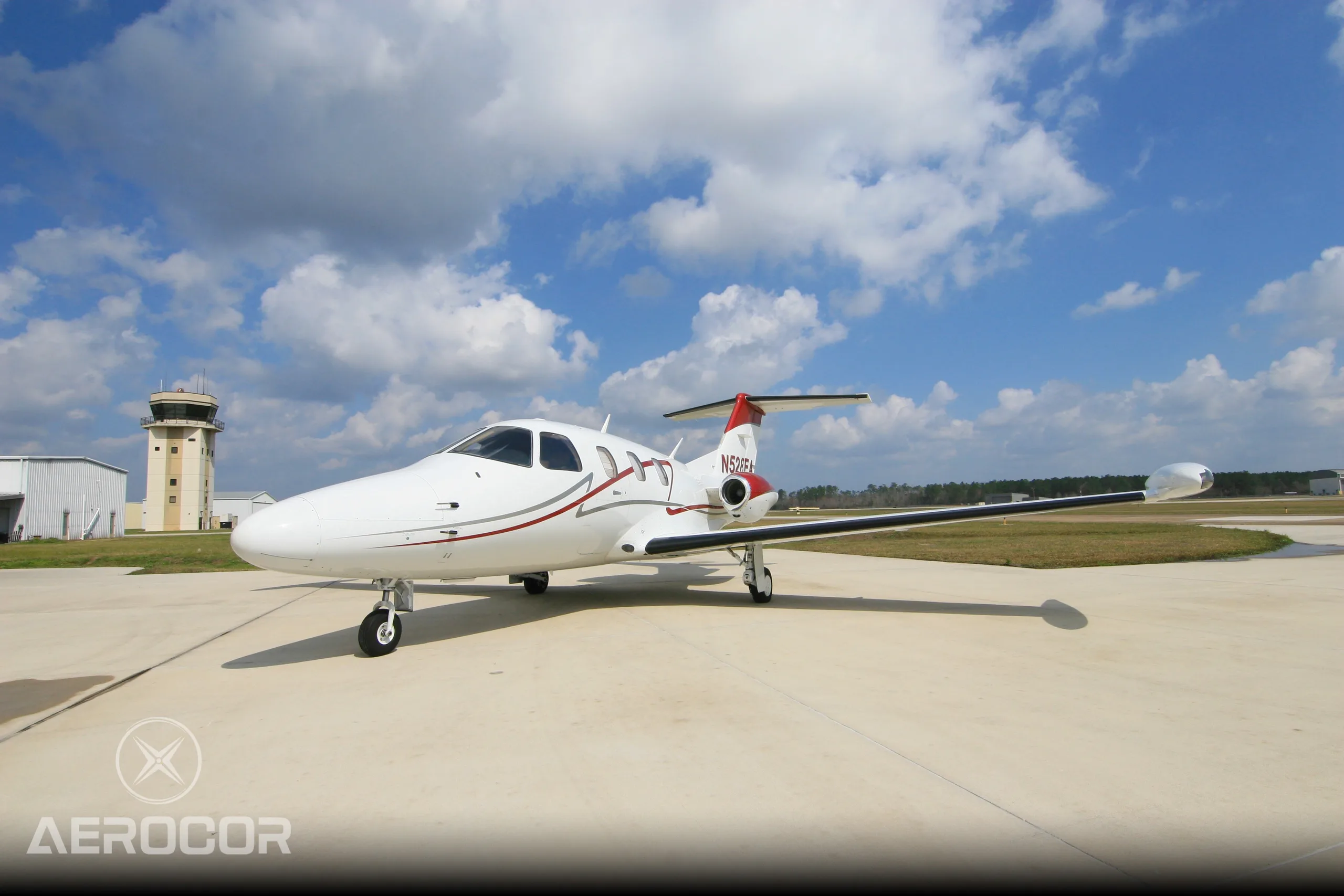 A white Eclipse 500 jet with red and grey stripes, registration N528EA, parked on an airport tarmac with a control tower in the background.