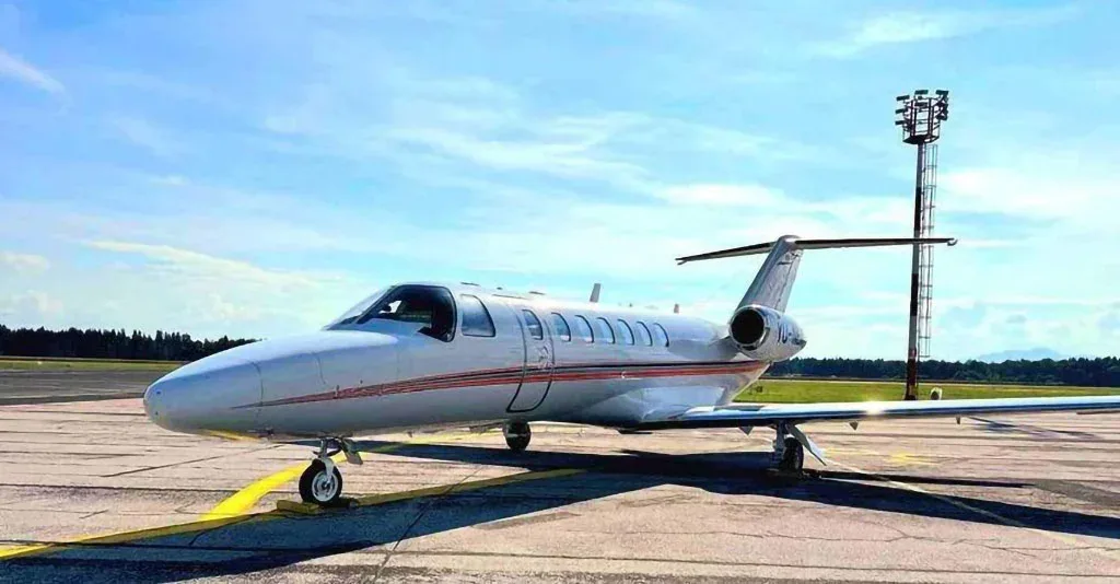 A white Cessna CitationJet with red stripes parked on an asphalt runway under a blue sky.