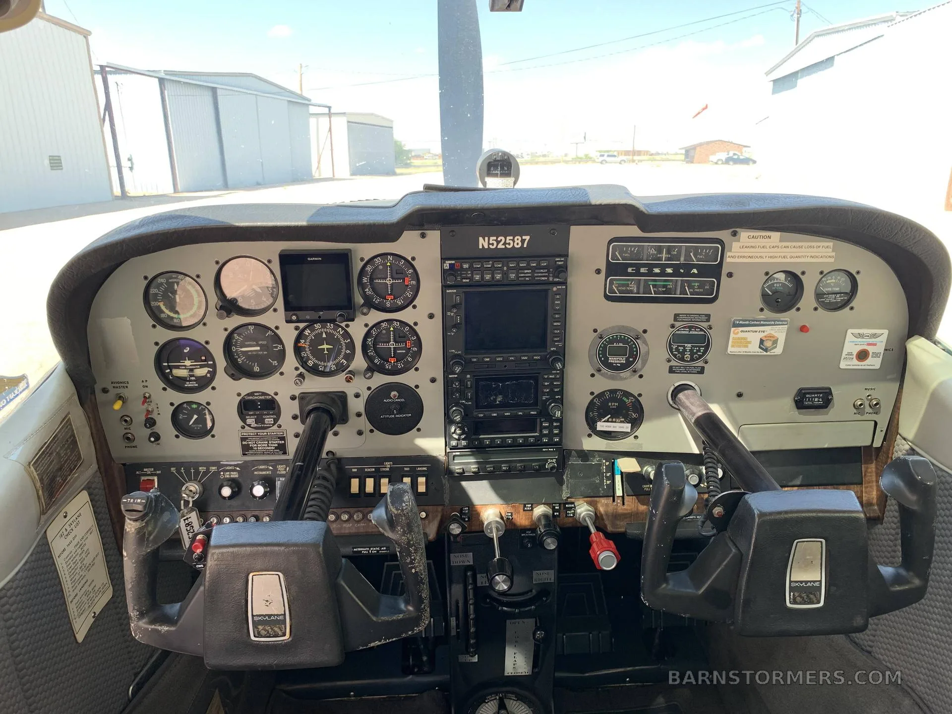 Wide view of a Cessna aircraft cockpit with analog gauges, two Garmin displays, and dual yokes.