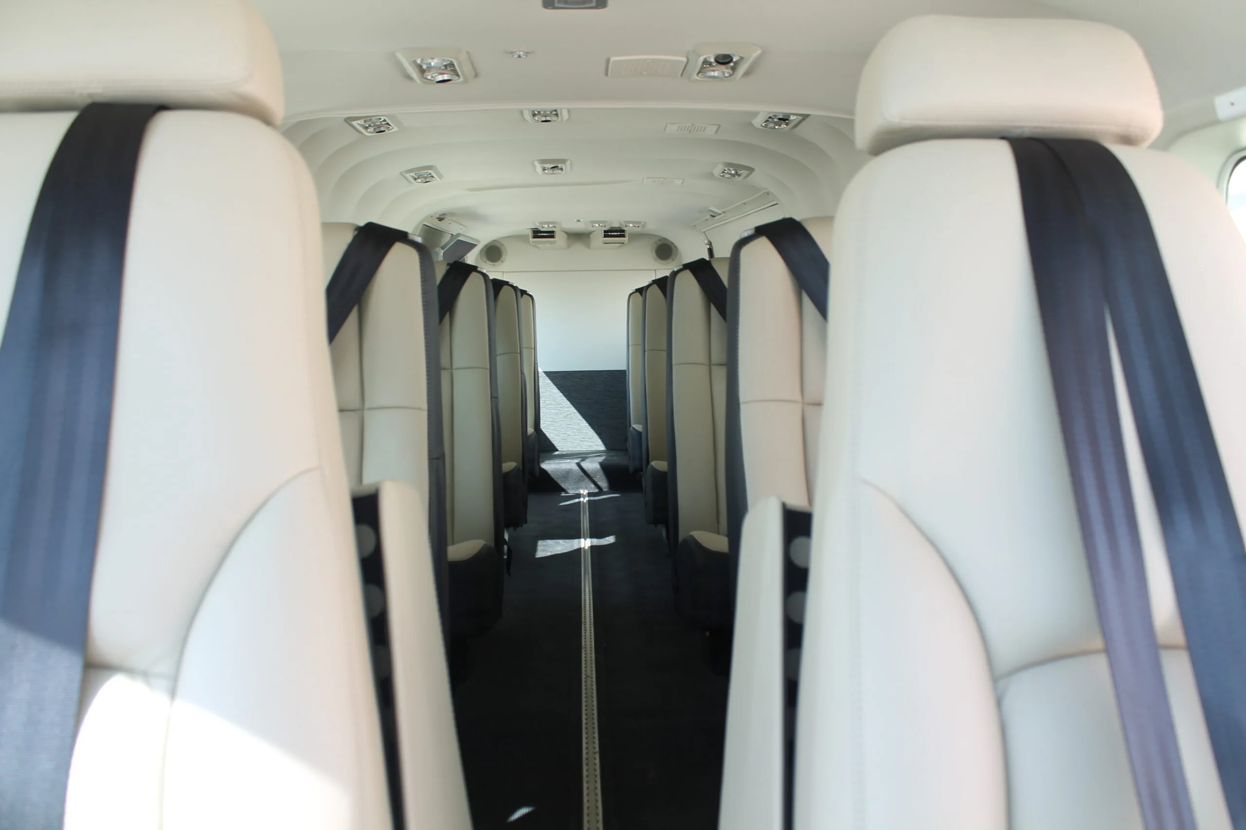 The aircraft cabin features rows of light-colored seats with dark seatbelts, looking towards the front.