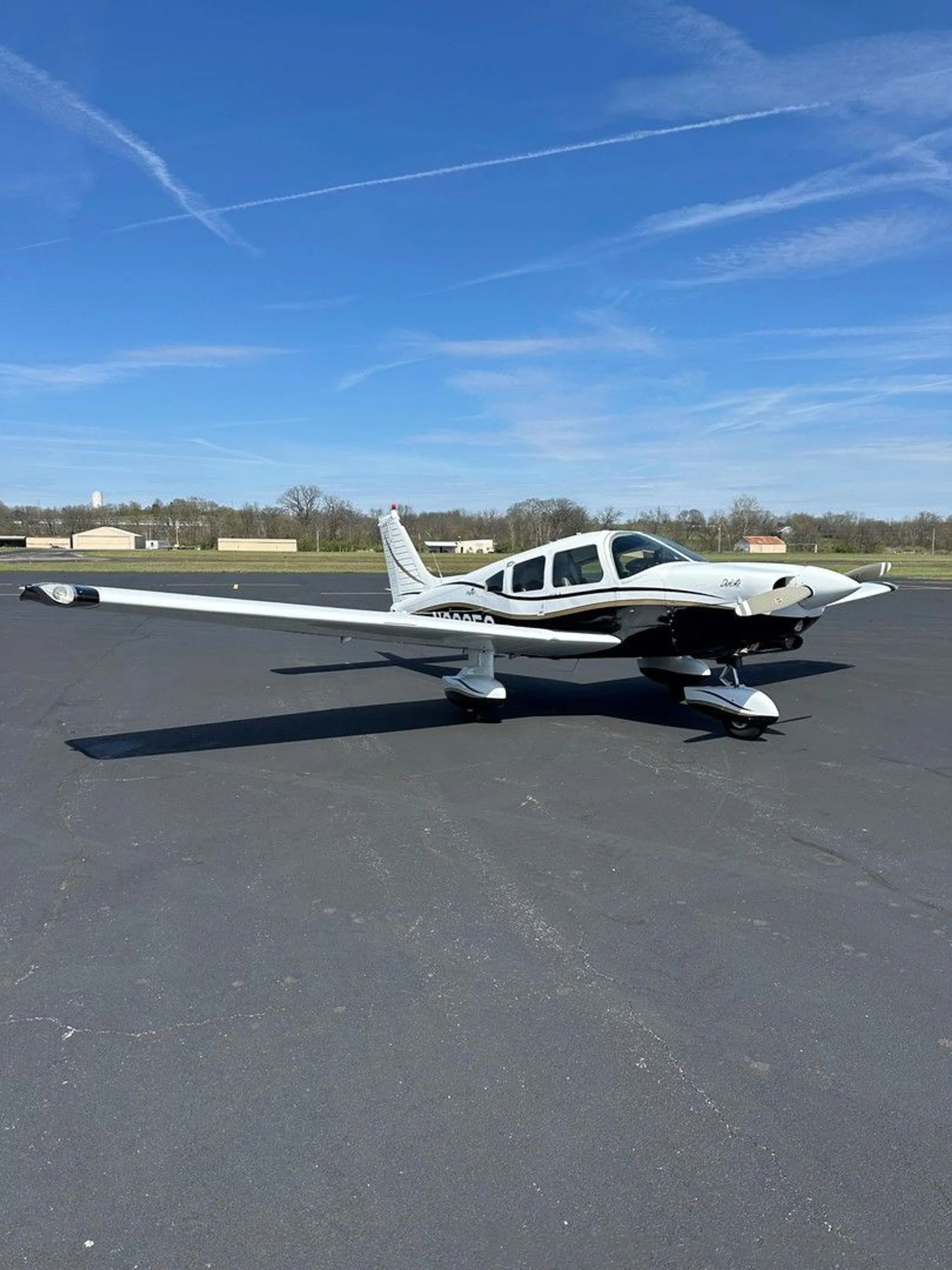 A white and black Piper aircraft with gold trim, registration N2235C, parked on an asphalt ramp under a blue sky.