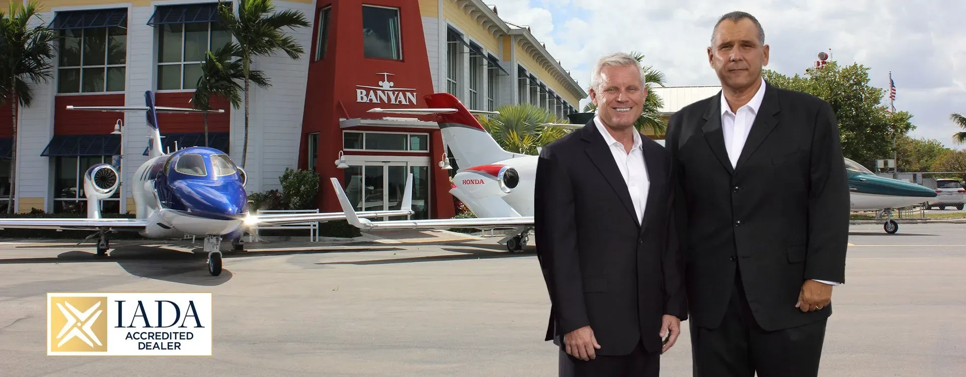 Two men stand in front of a Banyan FBO building with two HondaJet aircraft parked on the apron.