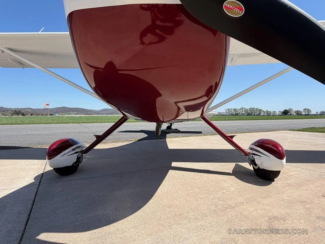 A low-angle view of the front of a white and maroon aircraft, showing the propeller, landing gear, and underside.