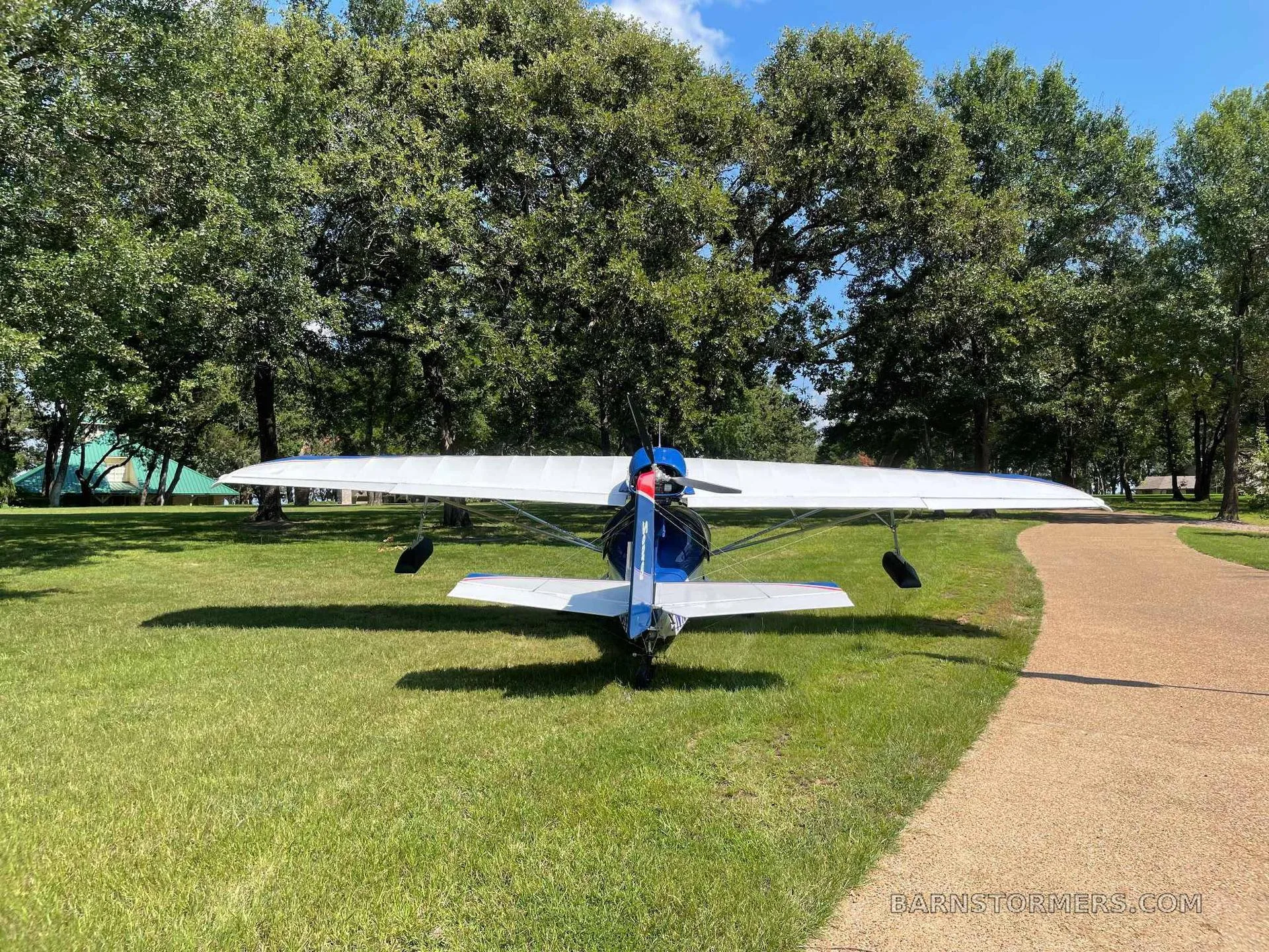 A rear view of a blue and white Searey amphibian aircraft with registration N167SR parked on grass next to a gravel path.