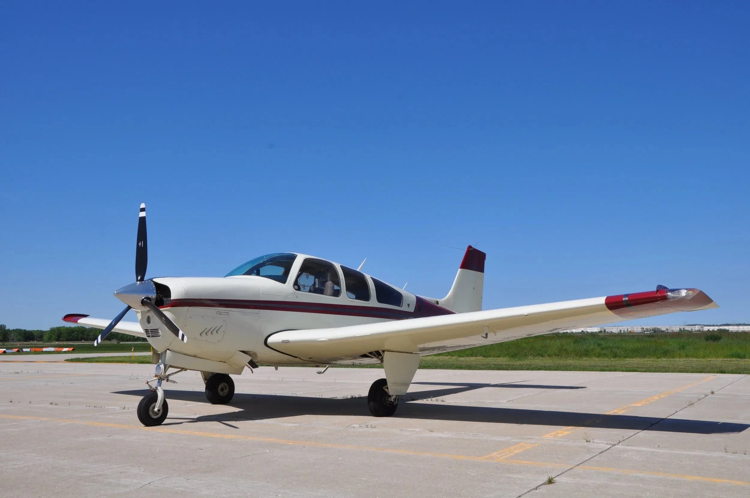 A white and maroon Beechcraft Bonanza F33A N159GM parked on a tarmac under a clear blue sky.