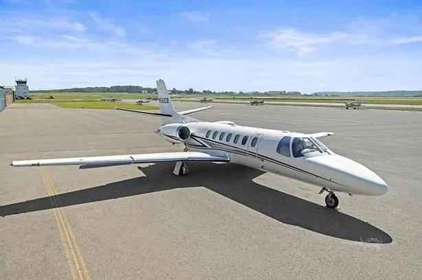 A white Cessna Citation CJ3 (N560CS) parked on an airport tarmac under a blue sky.