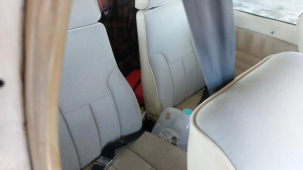 A close-up view of the light-colored aircraft seats in the cabin interior, with a water jug on the floor.