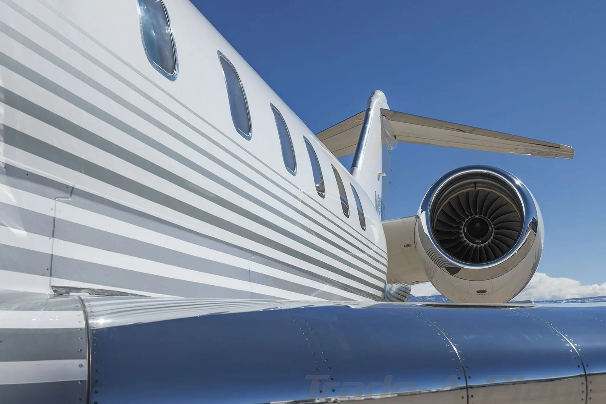 A close-up view of the right engine and wing of a white Bombardier Global 6000 business jet with grey pinstripes.