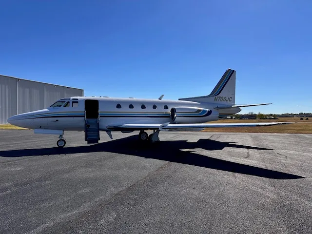 A full side view of the N700JC business jet with its airstair door open, showing its white fuselage with blue and gold stripes.