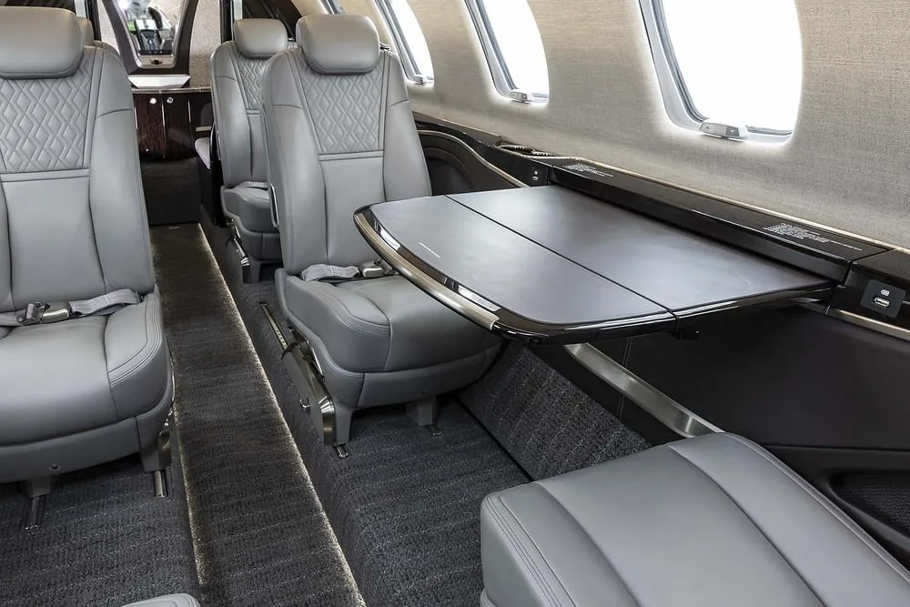 A close-up view of the aircraft's interior showing grey leather seats and a deployed side table.