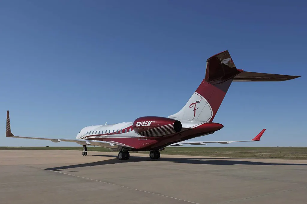 A Bombardier Global Express business jet with a white and maroon paint scheme, registration N919EM, viewed from the rear on a tarmac.