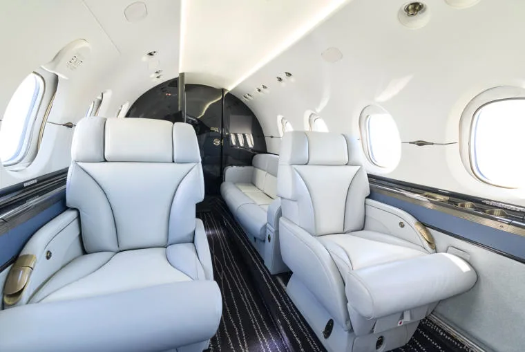 A view of the business jet's interior cabin, showing light grey leather club seats and a rear divan.