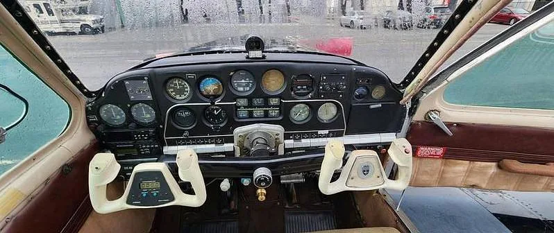 The cockpit of a small aircraft, showing the instrument panel with various gauges and two white control yokes.