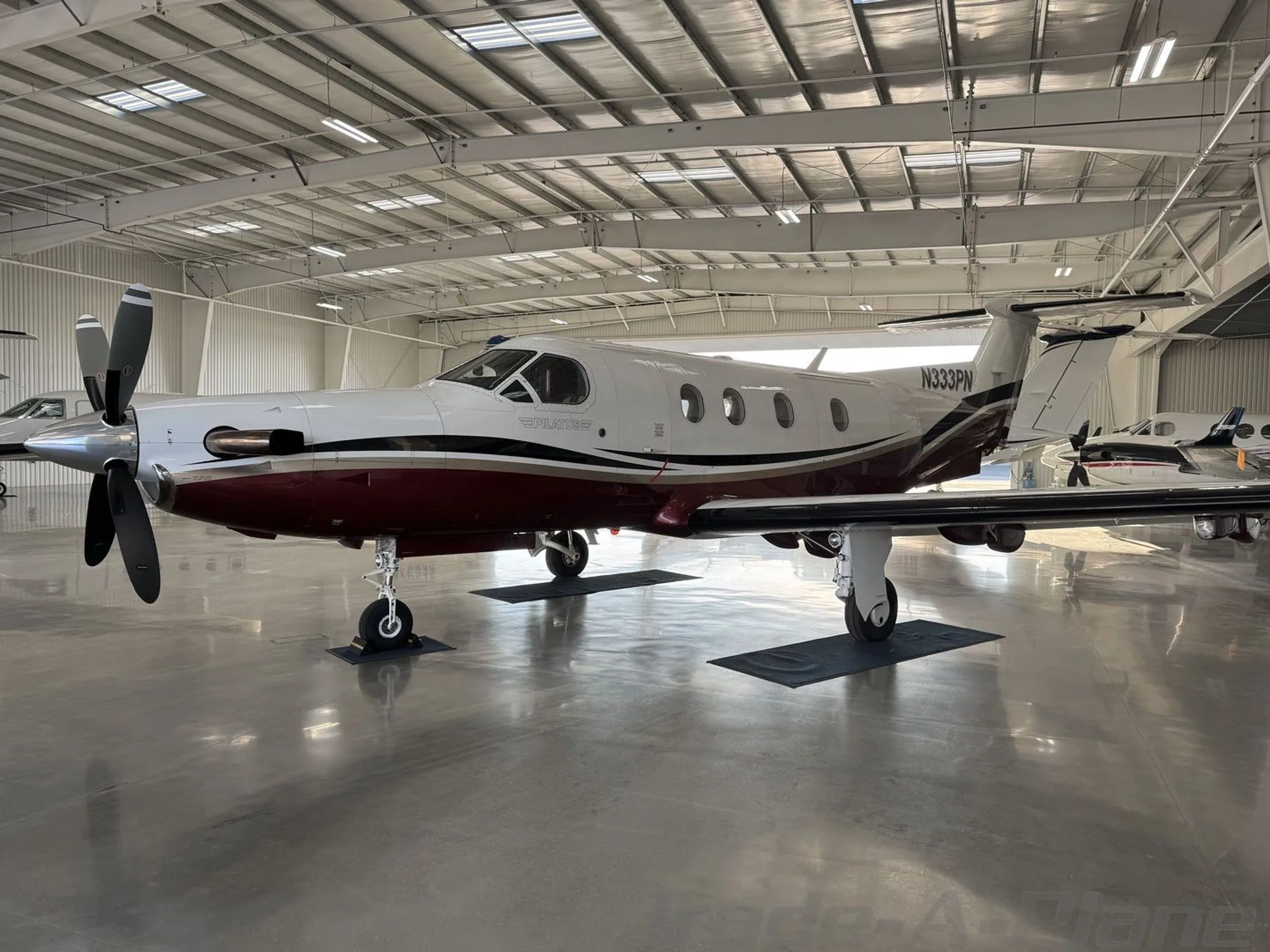 A Pilatus PC-12 turboprop aircraft with a white and maroon paint scheme, registration N333PN, parked in a hangar.