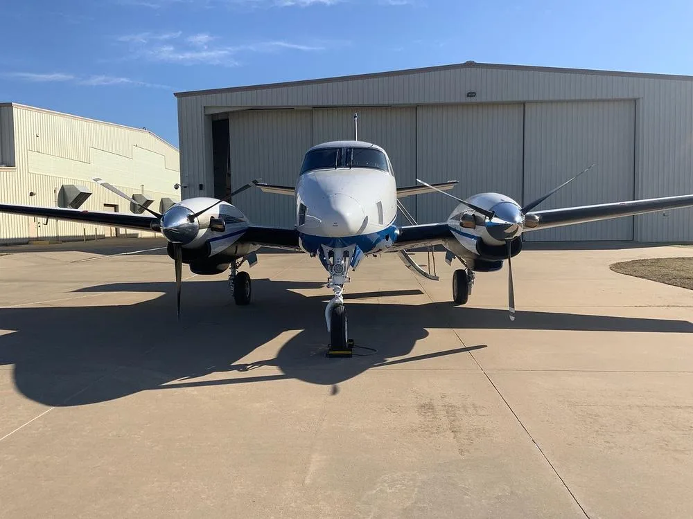 A head-on view of the white and blue twin-engine turboprop aircraft, N579PS, parked on an airfield.