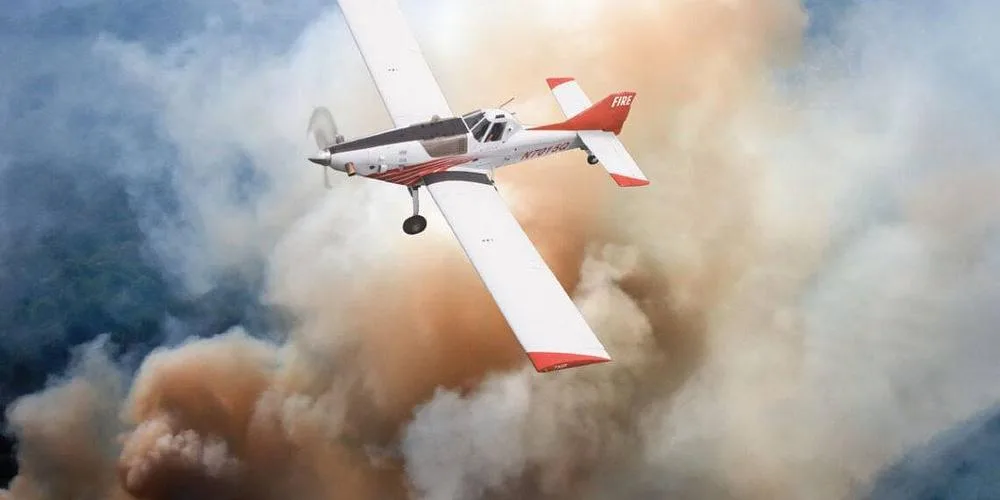 A white and red Thrush 510G aircraft with 'FIRE' on the tail, flying through dense smoke.