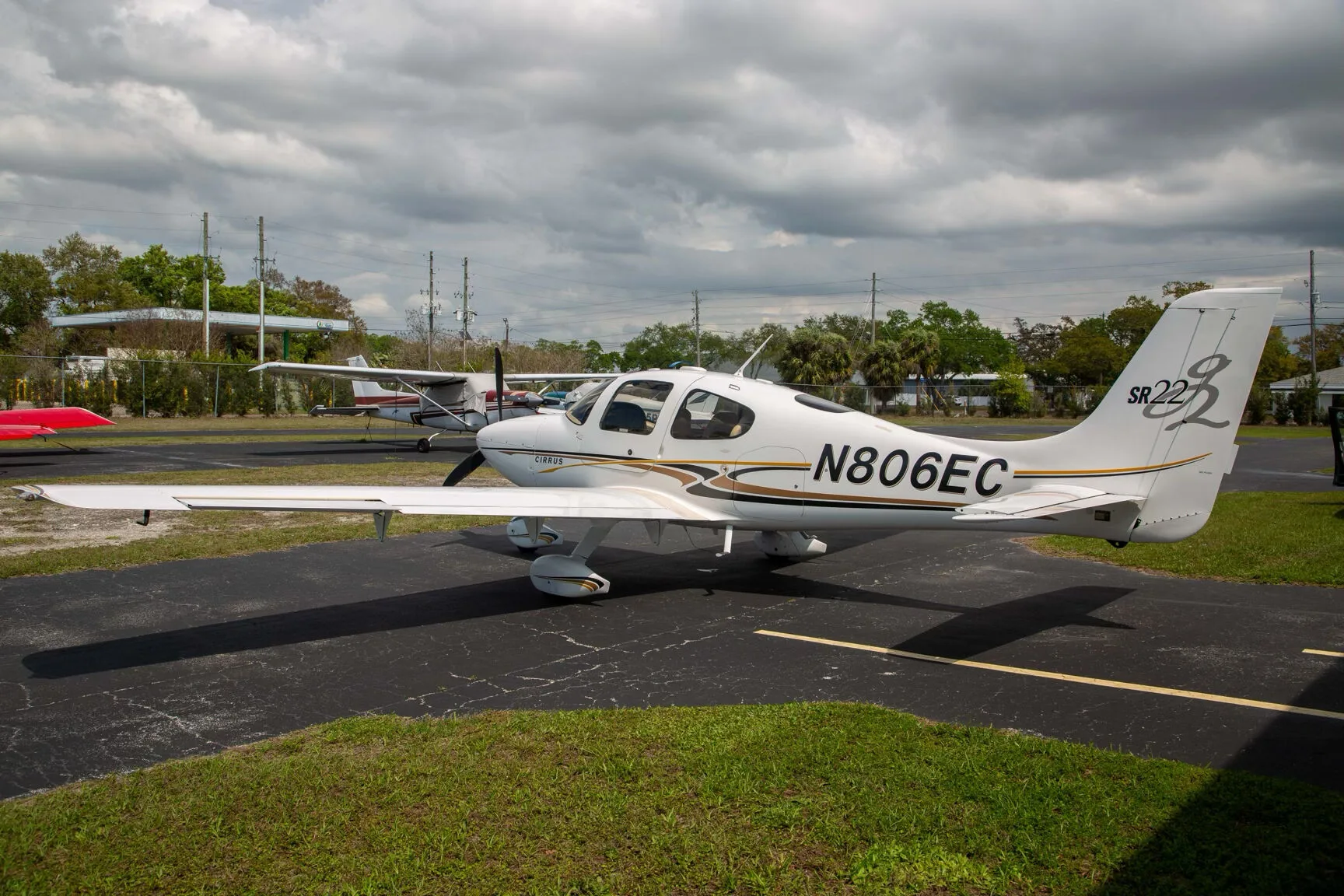 A white Cirrus SR22 aircraft with black and gold stripes, registration N806EC, parked on an asphalt tarmac.