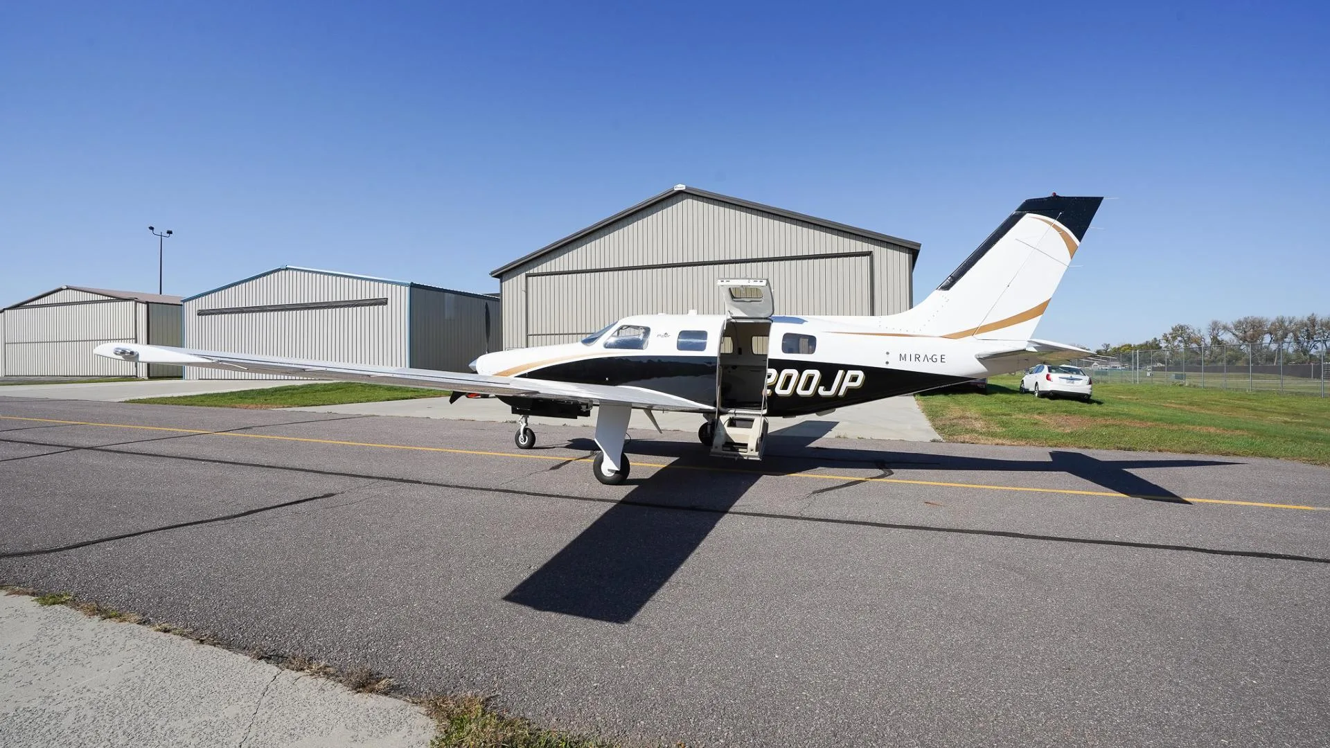 A white and black Piper Mirage N200JP with gold accents and open cabin door parked on an airfield.