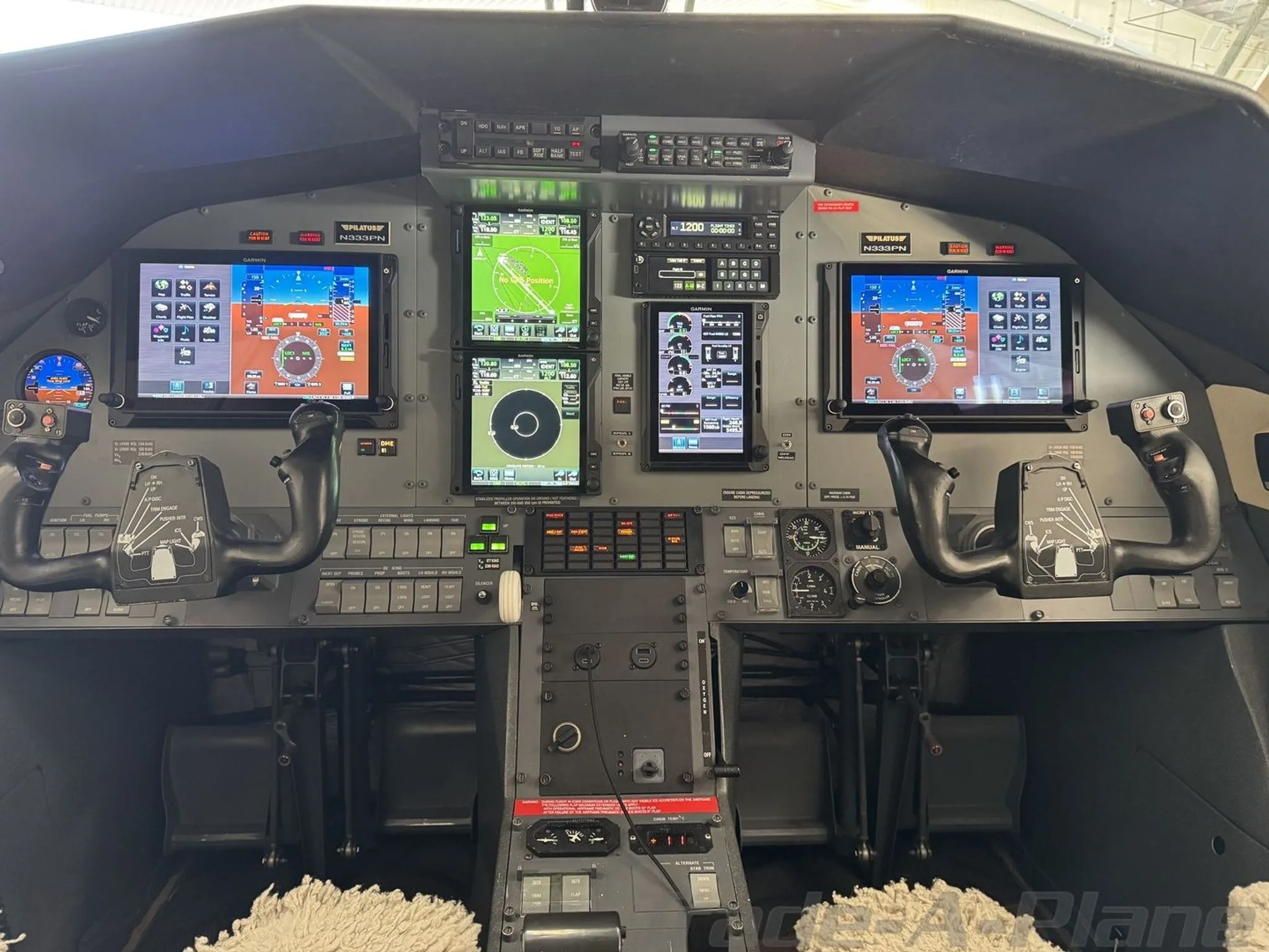 The cockpit of a Pilatus PC-12 aircraft, featuring multiple Garmin glass displays and dual yokes.