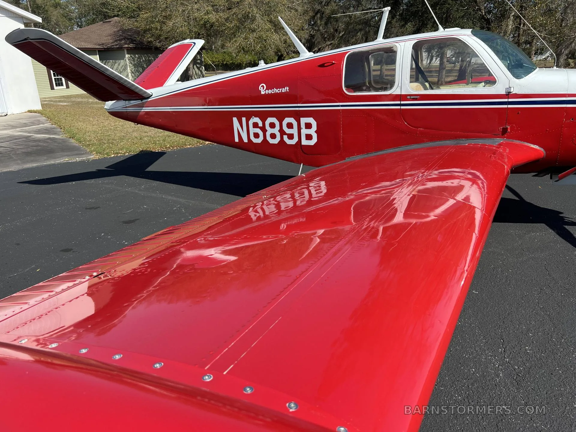 A close-up view of the red wing and fuselage of a Beechcraft Bonanza with registration N689B.