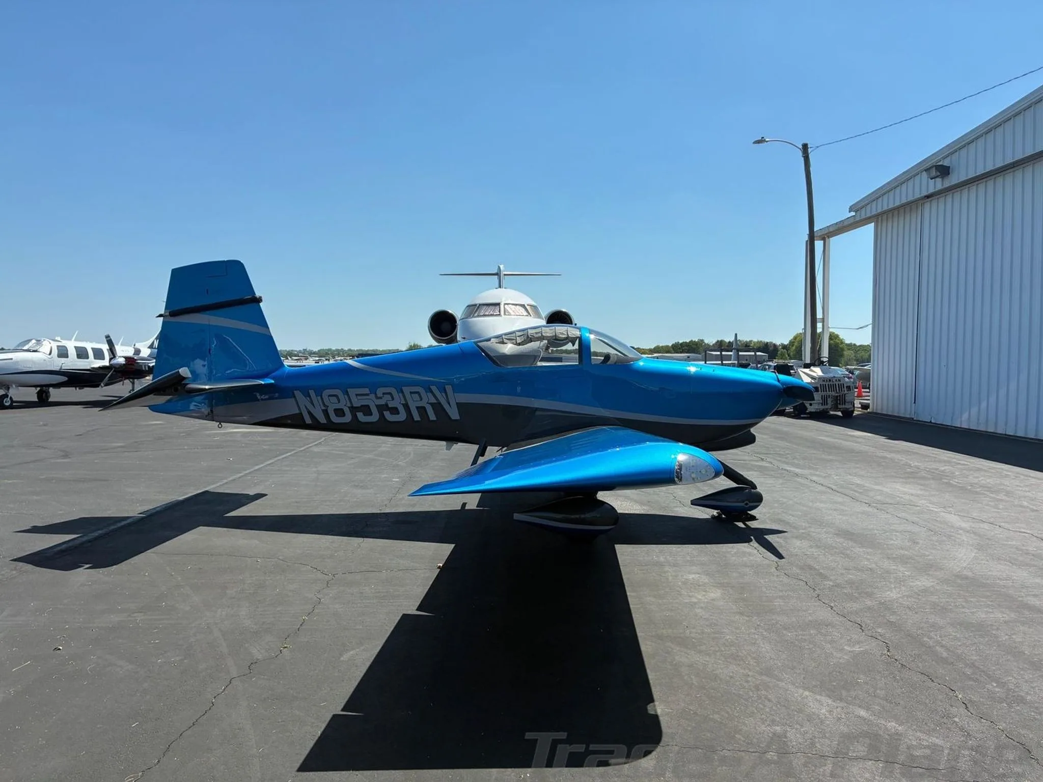 A blue and grey N853RV aircraft parked on an airfield next to a white hangar.