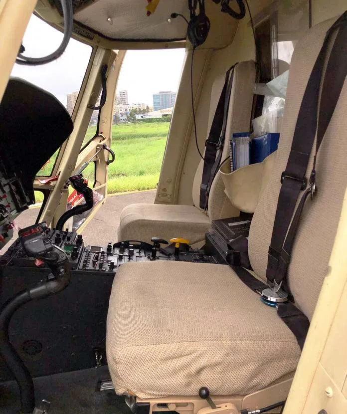 View from the side of a helicopter cockpit showing the pilot's seat, controls, and a partial view of the instrument panel.