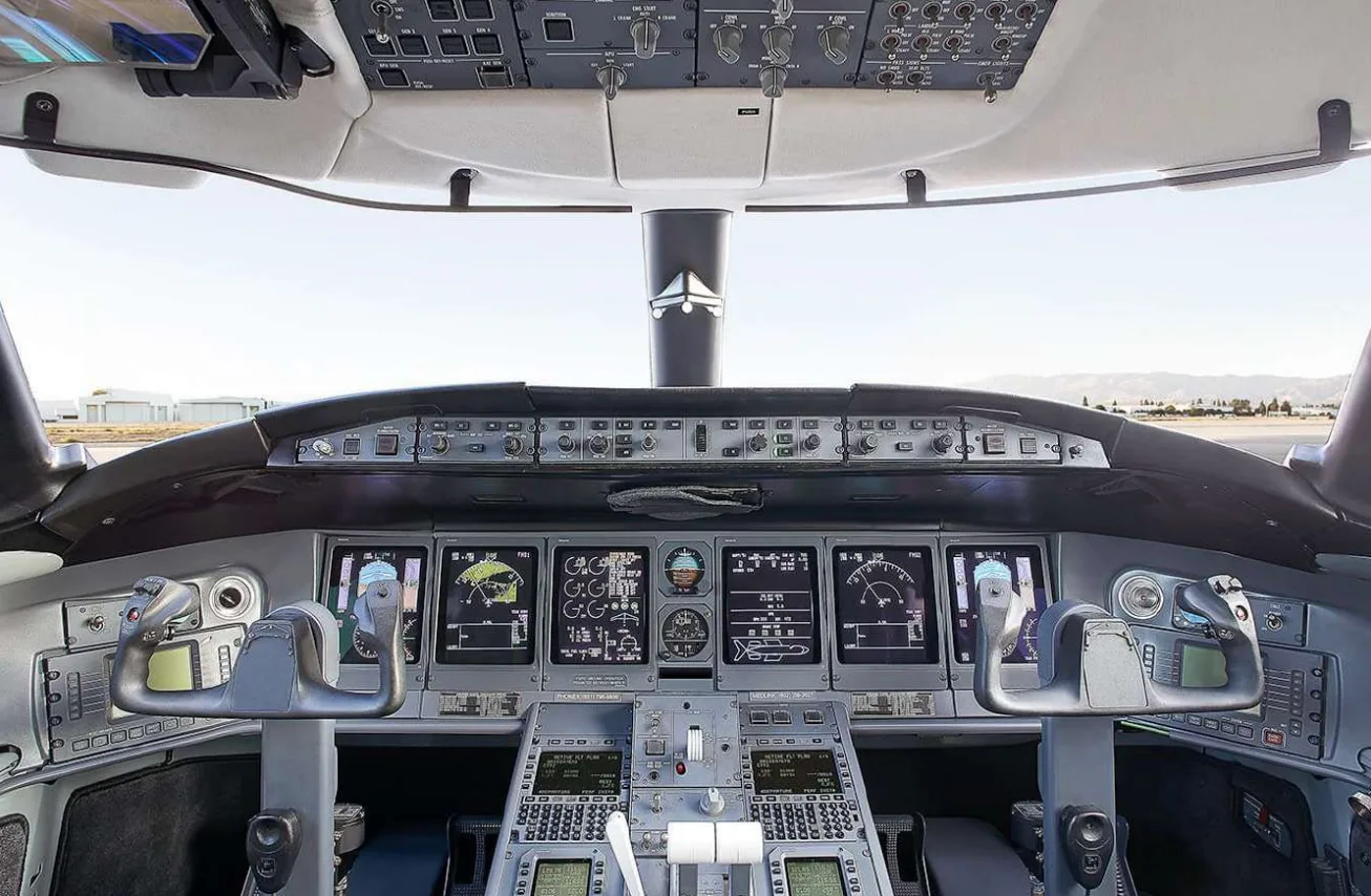 The modern cockpit of a private jet with multiple digital displays, control yokes, and an overhead panel.