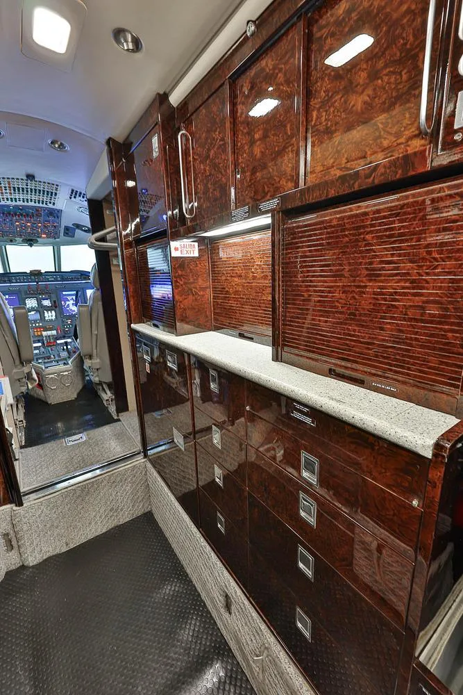 The aircraft's galley area with polished dark wood cabinetry, looking towards the cockpit.